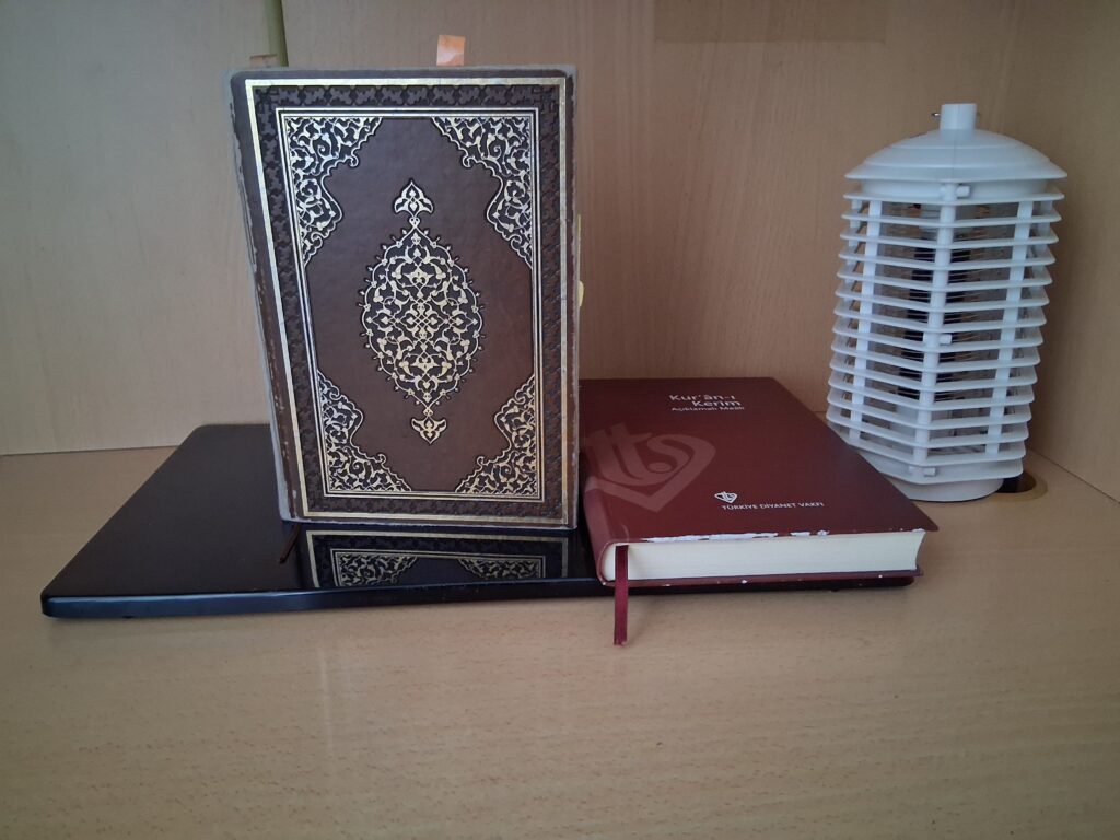 Evde namaz odası dekorasyonu için modern siyah rahle üzerinde Kur'an-ı Kerim, meal ve dekoratif fener.